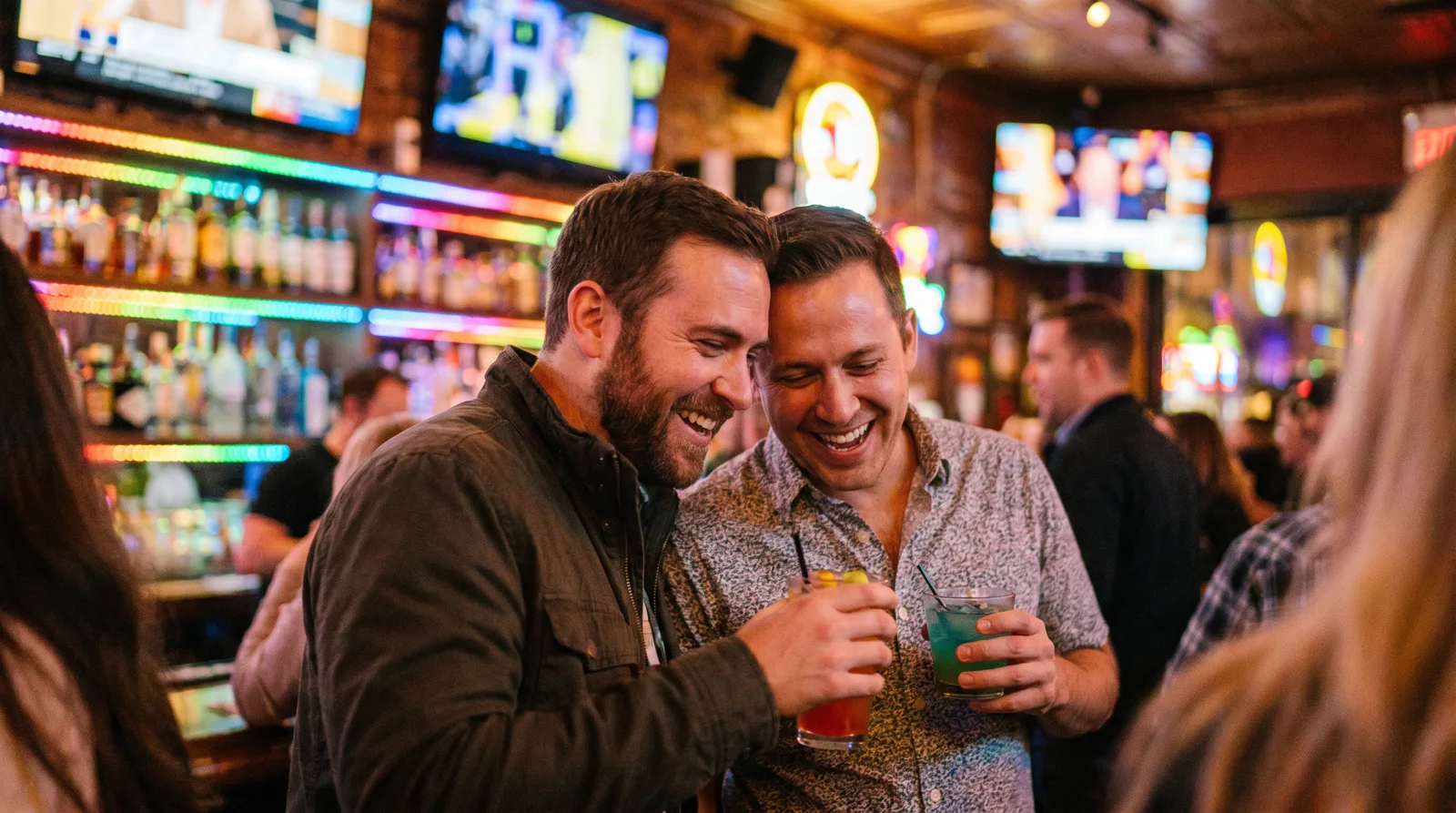 Two men laughing over cocktails at a stylish colorful bar