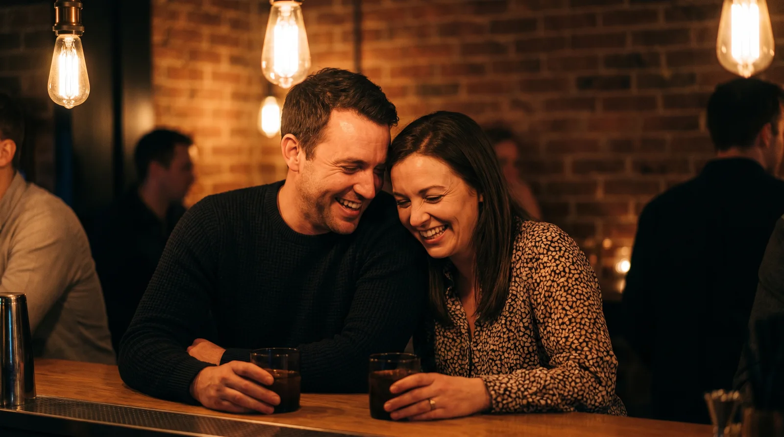 Man and woman laughing together over cocktails at a dimly lit Dallas cocktail bar
